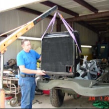 Man in blue shirt guiding halftrack radiator with crane and purple straps