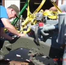 Two workers guiding engine into halftrack frame with yellow straps